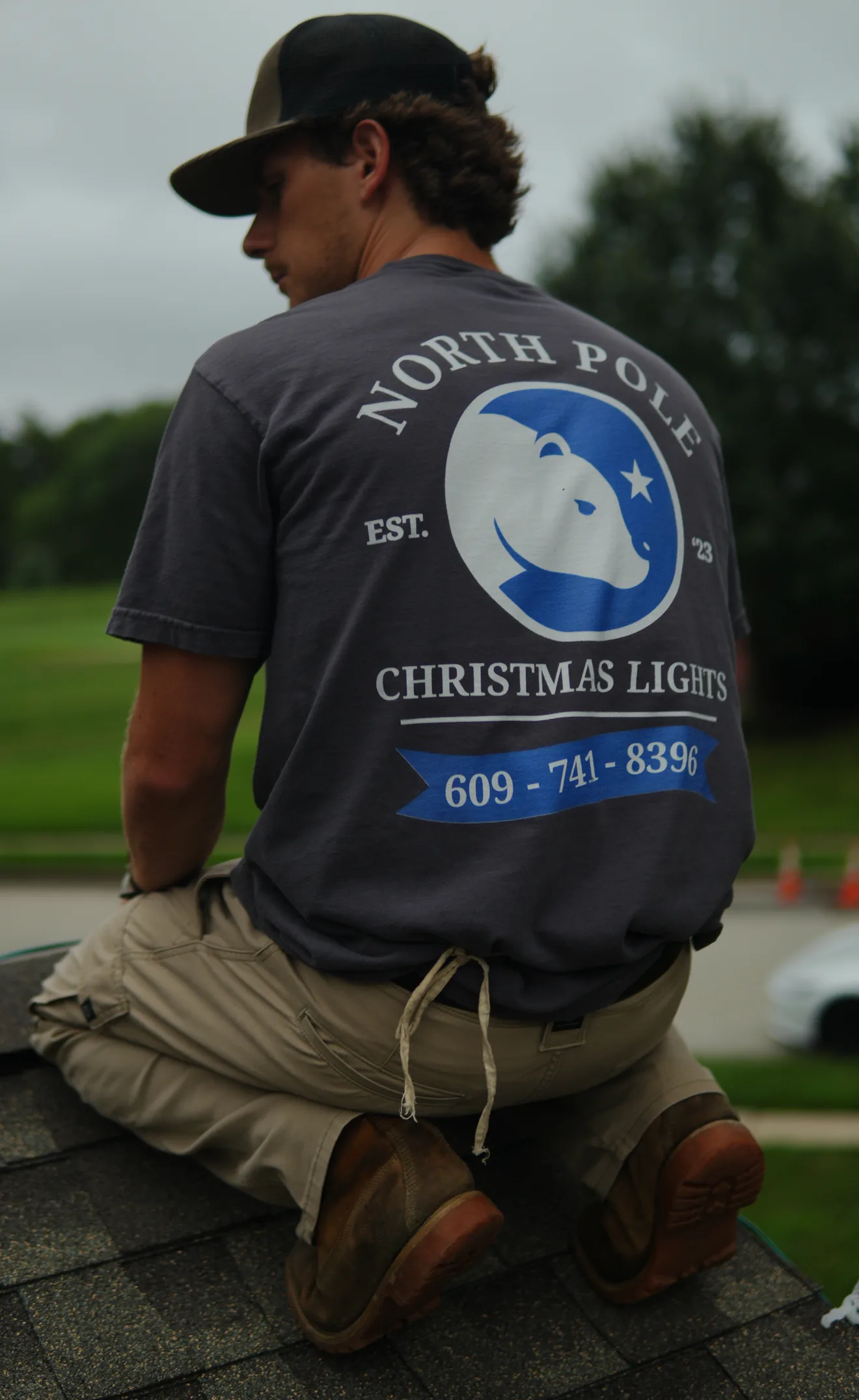 North Pole installers on a roof in branded shirts, the bear mark and phone number across the back